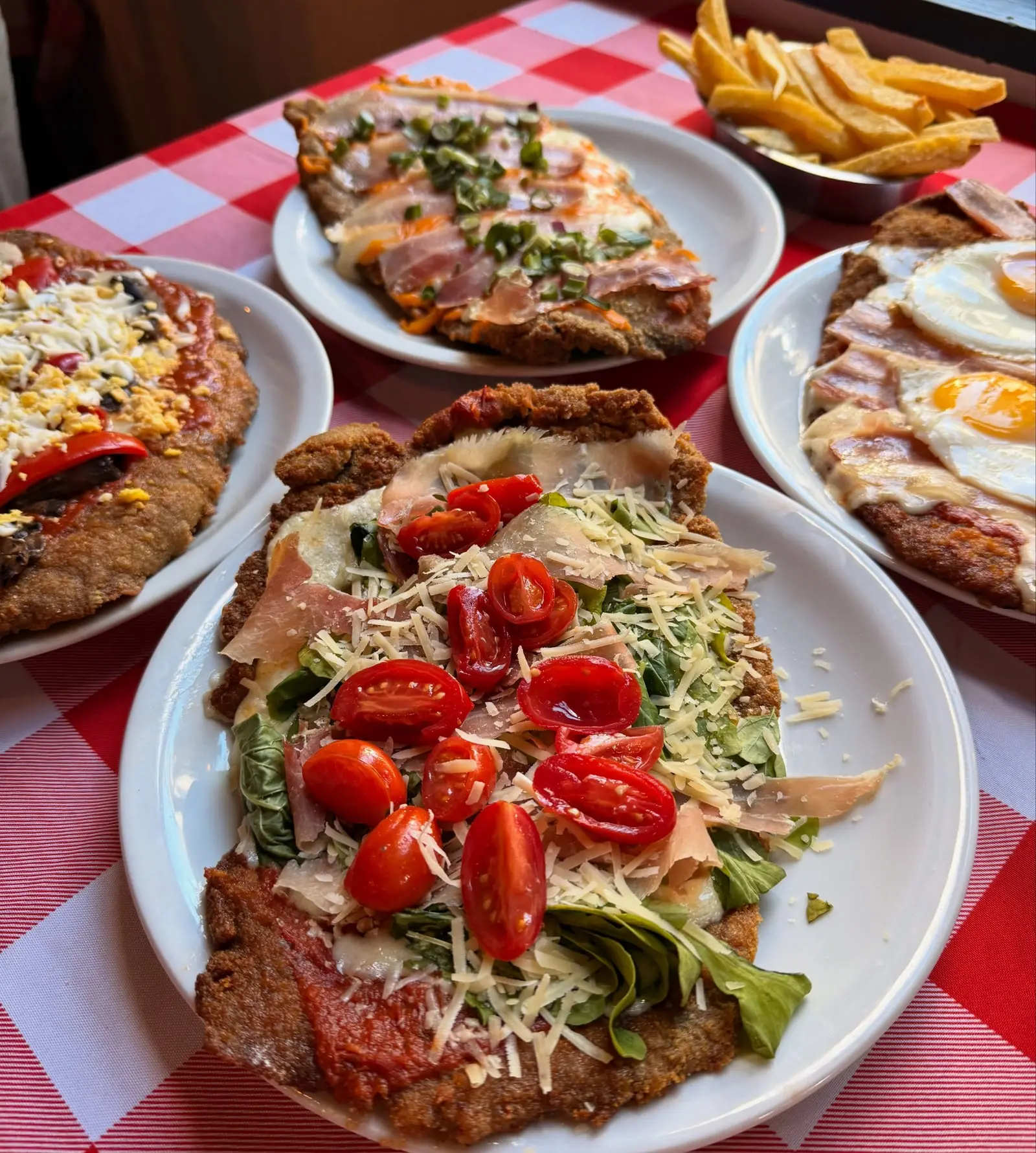 Mesa con cuatro milanesas gigantes de distintas variedades sobre mantel a cuadros